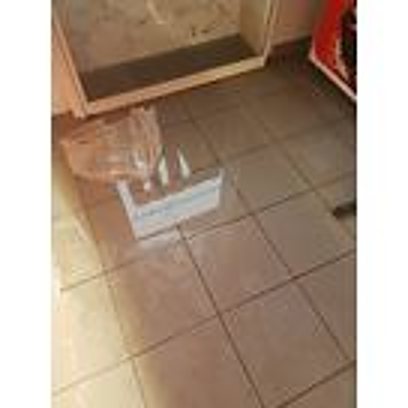 Un sol carrelé beige sur lequel est posée une boîte transparente avec une étiquette, devant une cabine de douche.