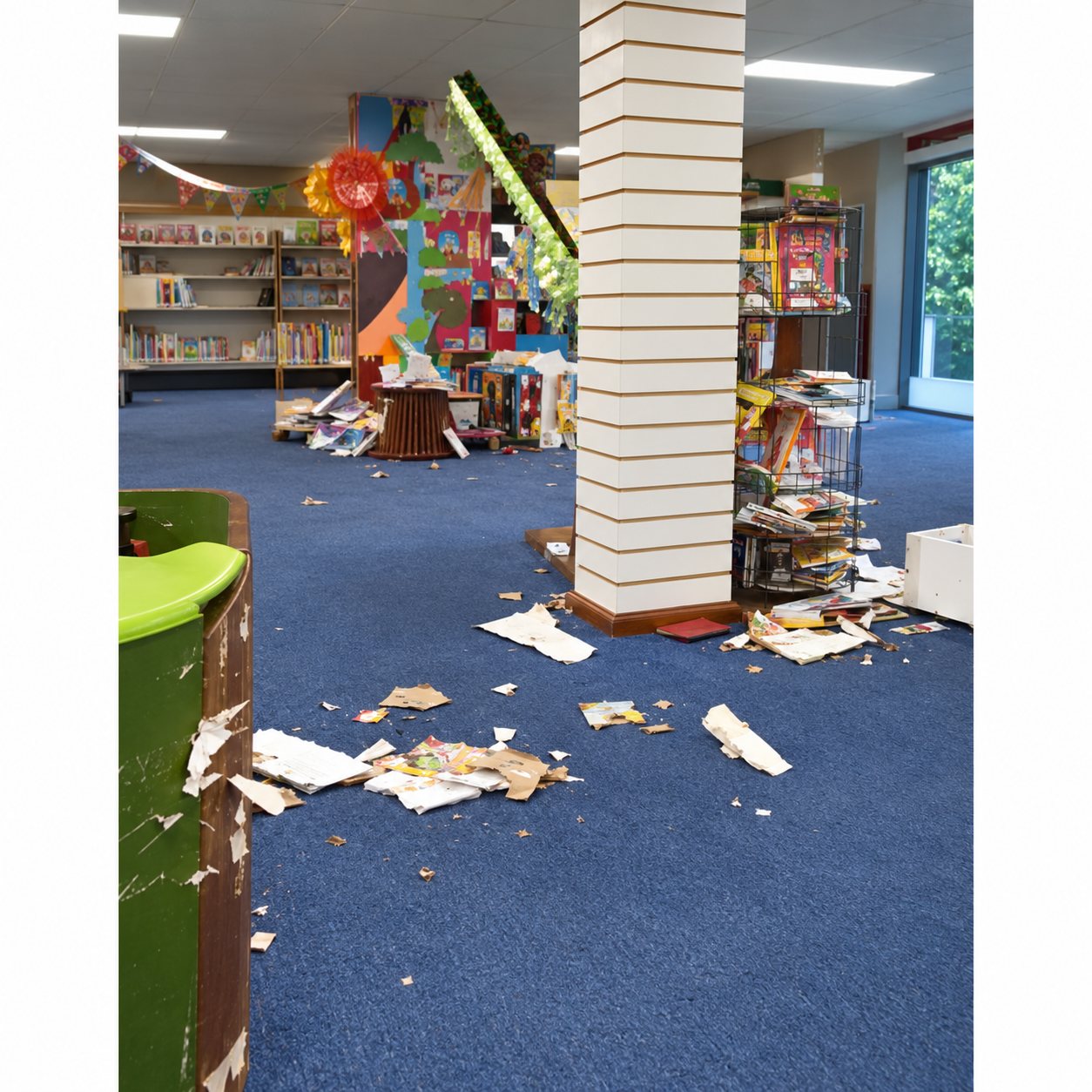 Intérieur d'un magasin à la moquette bleue dont le sol est jonché de papiers et de débris, avec des étagères en arrière-plan.