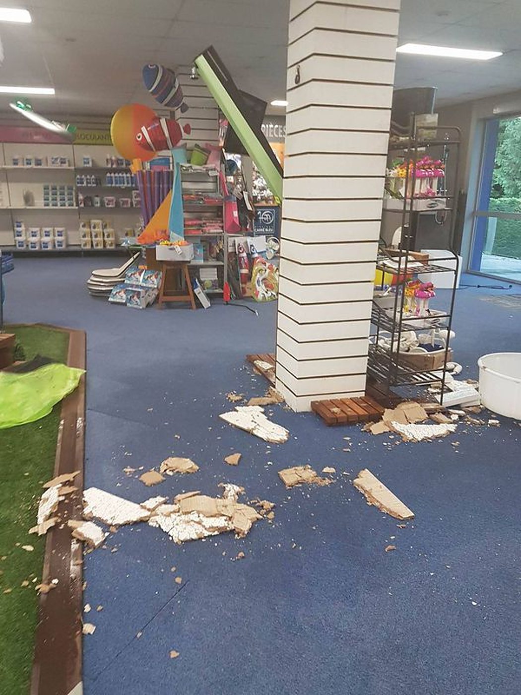 Intérieur d'un magasin d'articles de piscine où des morceaux de plafond effondrés jonchent la moquette bleue autour d'un pilier.